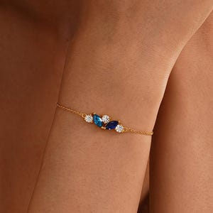 Könnte beinhalten: Ein zartes goldenes Armband mit einer Ansammlung blauer und weißer Edelsteine. Das Armband hat eine dünne Kette und ist mit Steinen im Marquise- und Rundschliff in Blau- und Weißtönen verziert.