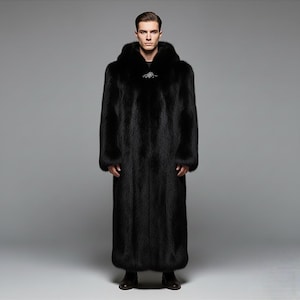 May include: Full-length black fur coat with a hood and a decorative clasp at the chest. The coat is floor-length and has long sleeves. The person is wearing black shoes. The background is a solid gray.