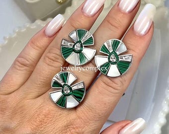 May include: Three silver-toned earrings with a fan-like design. Each earring features alternating sections of green and white, with a central green stone and surrounding clear crystals. The earrings are displayed on a hand.