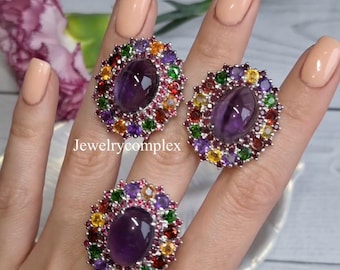 May include: Three silver rings featuring a large oval-cut purple amethyst center stone surrounded by a halo of smaller, multi-colored round gemstones including green, yellow, orange, and red stones. The text Jewelrycomplex is visible in the center.
