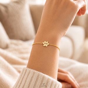 Puede incluir: Una pulsera de cadena en tono dorado con un dije central en forma de huella. El dije tiene grabado el nombre Leiko en letra cursiva. La pulsera está construida con una cadena de eslabones finos y se asegura alrededor de la muñeca con un cierre.