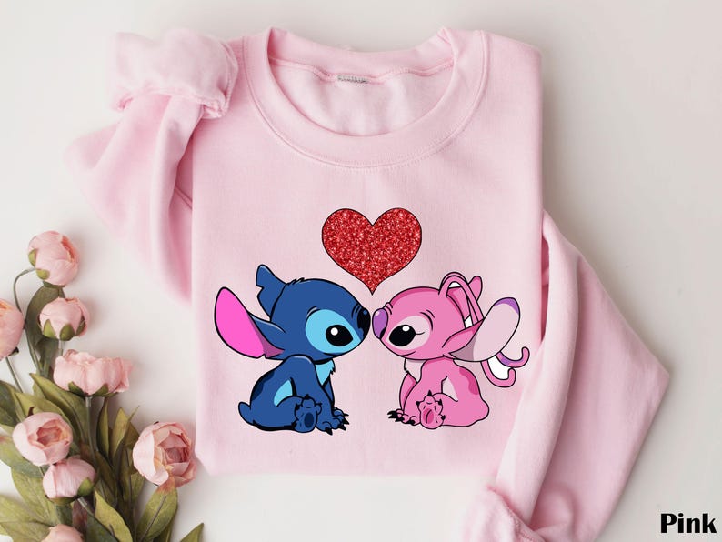 A pink sweatshirt with a graphic of two cartoon characters, a blue one and a pink one, sitting next to each other and a heart in the center.