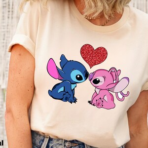 A person wearing a white t-shirt with a graphic of two cartoon characters, a blue one and a pink one, sitting together and having a heart between them.