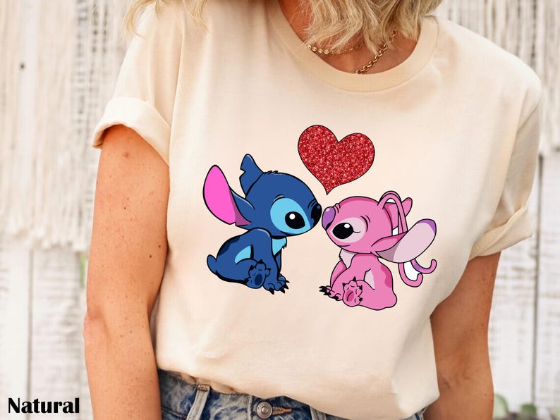 A person wearing a white t-shirt with a graphic of two cartoon characters, a blue one and a pink one, sitting together and having a heart between them.