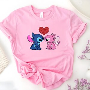 A pink t-shirt with a graphic of two cartoon characters, a blue one and a pink one, with a heart between them.