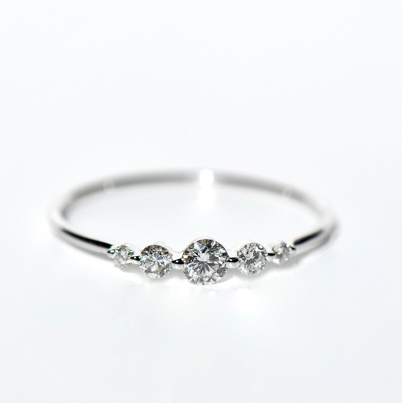 May include: A delicate silver ring with five small round diamonds set in a curved line.
