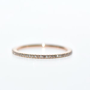 Puede incluir: Un anillo de banda de oro rosa con peque&ntilde;as piedras preciosas transparentes engastadas alrededor de toda la circunferencia. El anillo est&aacute; sobre un fondo blanco brillante, resaltando el brillo de las piedras preciosas. Este anillo es una joya fina.