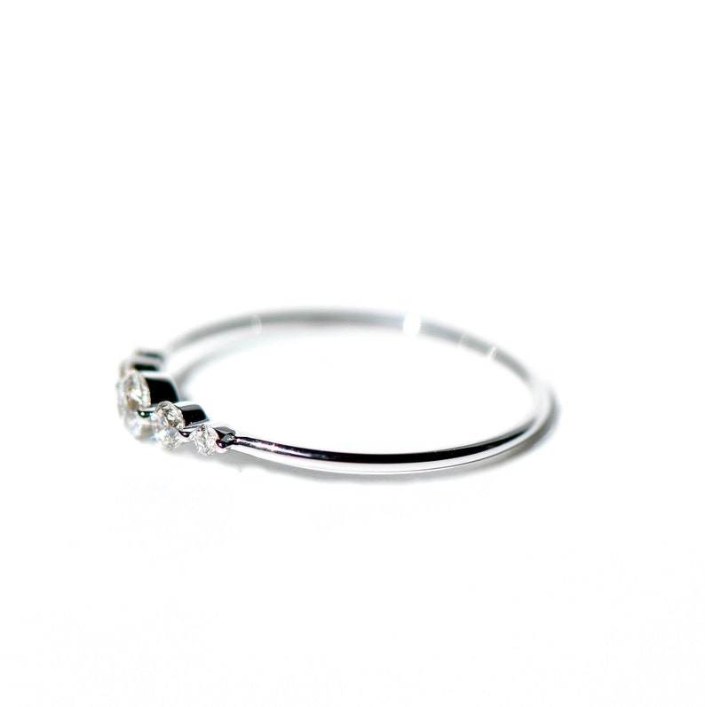 May include: A delicate silver ring with a row of small, clear gemstones set along the band.