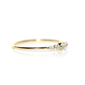 May include: A delicate gold band ring with a cluster of small, clear diamonds set in a curved line.