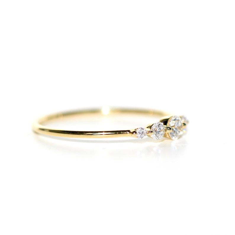 May include: A delicate gold band ring with a cluster of small, clear diamonds set in a curved line.
