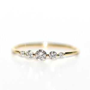 May include: A delicate gold band ring with five round diamonds set in a row. The diamonds are graduated in size, with the largest diamond in the center.