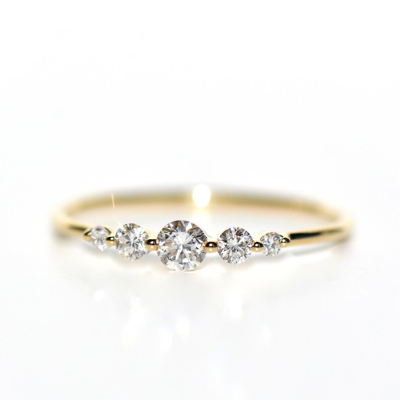 May include: A delicate gold band ring with five round diamonds set in a row. The diamonds are graduated in size, with the largest diamond in the center.