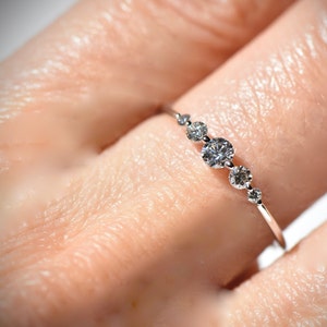 May include: A delicate silver ring with a row of five small, round diamonds set in a graduated size.