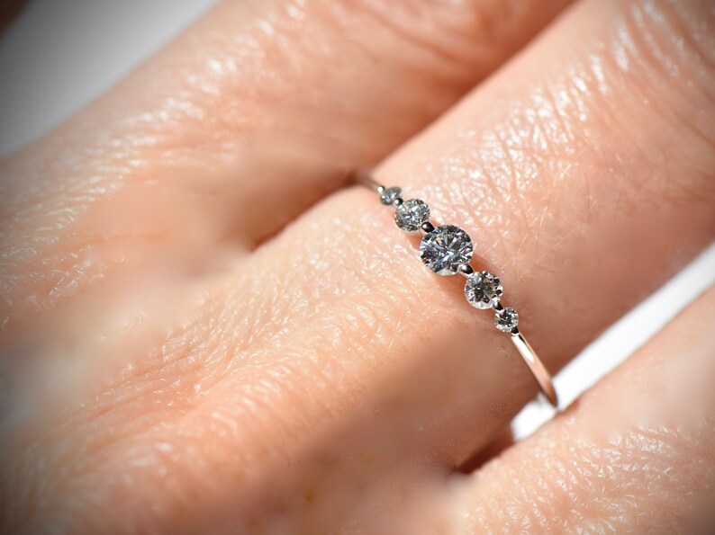 May include: A delicate silver ring with a row of five small, round diamonds set in a graduated size.