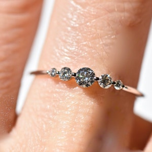 May include: A delicate silver ring with five small round diamonds set in a row. The ring is worn on a finger.