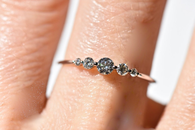 May include: A delicate silver ring with five small round diamonds set in a row. The ring is worn on a finger.