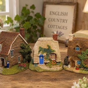 May include: Three miniature cottage figurines featuring detailed architectural elements. The left house has brown siding and a red roof. The center house has a thatched roof and a blue door. The right house has a textured brown roof and stone walls.