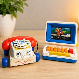 Pode incluir: Dois telefones de brinquedo vintage. Um é um telefone rotativo vermelho e branco com rodas azuis. O outro é um computador de brinquedo azul e branco com teclas laranja e uma tela exibindo uma cena de cavalo. A palavra "horse" é exibida.