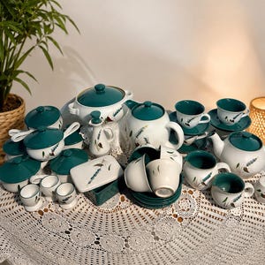 May include: A large ceramic dinnerware set featuring white pieces with deep teal lids and accents, decorated with small painted wheat stalks. The collection includes teapots, lidded tureens, cups, saucers, a creamer, a butter dish, and egg cups.