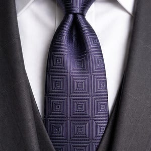 May include: A close-up shot of a dark purple tie featuring a geometric square pattern, worn with a white shirt and a dark grey suit jacket. The tie's design is a repeating series of squares within squares.