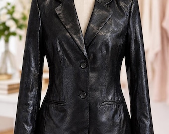 Op de afbeelding: Een zwarte blazer met een getextureerd, op slangenleer lijkend patroon. De blazer heeft een gekerfde revers, twee knopen en twee voorzakken. Het wordt op een mannequin getoond.