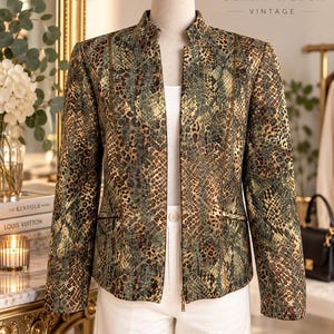 May include: A Gerry Weber Vintage jacket featuring a green, brown, and gold snakeskin pattern. The jacket has a stand-up collar, long sleeves, a front zip closure, and two horizontal welt pockets. It is displayed on a mannequin over a white top.