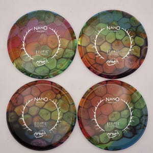 Pode incluir: Quatro mini discos Nano circulares feitos de plástico brilhante Eclipse, cada um com um padrão de favo de mel multicolorido vibrante. O centro de cada disco exibe o texto Nano Mini Disc, Eclipse Glow Plastic e o logotipo MVP Disc Sports.
