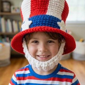 Puede incluir: Un niño con un sombrero de ganchillo de Uncle Sam rojo, blanco y azul con barba a juego. El sombrero tiene un ala roja, una banda azul con estrellas blancas y rayas rojas y blancas. El niño también lleva una camiseta a rayas rojas, blancas y azules.
