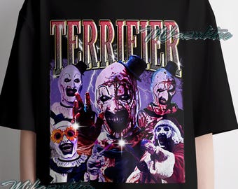 May include: Black t-shirt featuring a graphic of several terrifying clowns with the word "TERRIFIER" in a red and gold font. The clowns have white faces, dark eye makeup, and blood. The shirt is a crew neck.