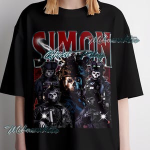 Könnte beinhalten: Schwarzes T-Shirt mit einem grafischen Design mit dem Text "SIMON Ghost Riley" in Rot und Blau. Das Design enthält Bilder von maskierten Figuren in taktischer Ausrüstung, wodurch eine militärische oder actionorientierte Ästhetik entsteht.