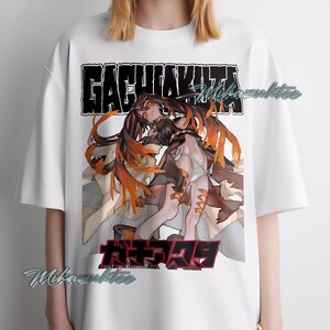 May include: White t-shirt featuring a graphic design with the text "GACHIAKITA" above and Japanese text below. The graphic depicts two figures with long hair and orange accents.