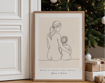 May include: A framed line art print featuring a mother and child embracing. The artwork is in black lines on a beige background, with the text "WHERE MY HEART FEELS WHOLE" and a signature below. The frame is light brown.