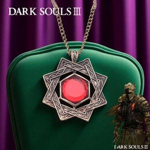 May include: A silver-colored pendant necklace with a red gemstone center, featuring an intricate Celtic knot design. The necklace hangs on a chain. The words "DARK SOULS III" are at the top of the image.