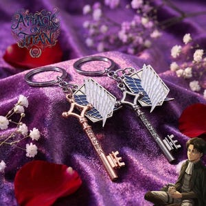 May include: Two keychains featuring a key design and the Survey Corps emblem from the anime Attack on Titan. One key is gold-coloured, the other silver. The keychains rest on a purple velvet surface with white flowers and rose petals.