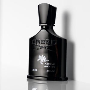 May include: A black perfume bottle with a matte finish. The bottle has a rectangular shape with a rounded base and a tall, cylindrical cap. The word "CREED" is embossed on the front, along with the words "ABSOLU AVENTUS", and "75 ml / 2.5 fl.oz."