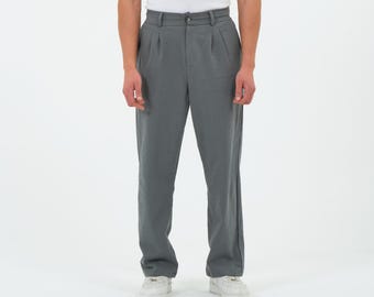 May include: Gray pleated trousers with a button closure and a straight leg. The pants are made of a lightweight fabric and are worn with white sneakers. The trousers have a classic, tailored look.