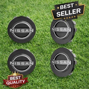 May include: Four black Nissan hubcaps with a silver ring and the Nissan logo in silver. The hubcaps are on a green grassy surface. Two stickers read "Best Seller" and "Best Quality".