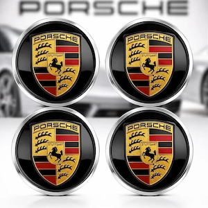 May include: A set of four circular Porsche emblem wheel center caps featuring the iconic crest with a black horse, red and black horizontal stripes, and gold background. Each emblem is encased in a polished silver metallic ring border.