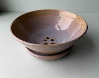 Op de afbeelding: Een keramische kom met bijpassende schotel. De rand van de kom is lichtbruin, overgaand in een lavendelroze tint in het midden. Het heeft drainagegaten en een glanzende afwerking. Ideaal voor planten.