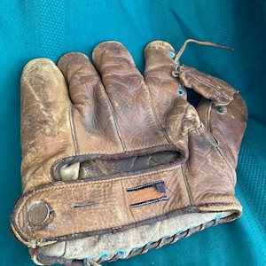 May include: A brown leather baseball mitt with a blue and white lacing detail. The mitt has a strap with a circular logo and a brown leather patch.