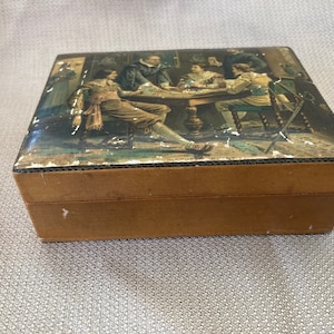 May include: A wooden box with a hinged lid. The lid is decorated with a vintage illustration of five men sitting around a table playing cards. The box is brown and has a distressed look.