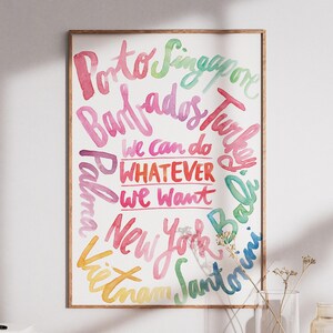 Könnte beinhalten: Ein rechteckiger Wandkunstdruck in einem Holzrahmen mit aquarellartigem Text in verschiedenen Farben. Der zentrale Text lautet "we can do WHATEVER we want", umgeben von einer kreisförmigen Anordnung von Stadt- und Ländernamen wie Porto, Singapore, Barbados, Turkey, Bali, Santorini, Vietnam, New York und Palma.