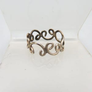 May include: A silver-colored ring with a continuous, swirling design. The ring's pattern features a series of interconnected, flowing curves, creating an openwork effect. The ring is likely made of sterling silver or a similar metal.
