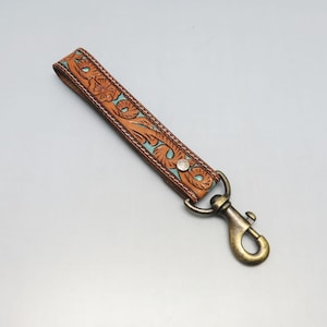 May include: A brown leather key chain with a turquoise floral design and a brass hook.