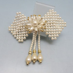 以下が含まれることがあります： 花柄と3本の真珠のドロップストランドが付いた白い真珠のヘアクリップ