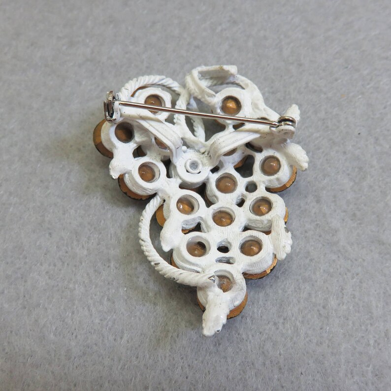 May include: White metal brooch with a grape cluster design. The grapes are made of clear glass with gold accents. The brooch has a pin back.
