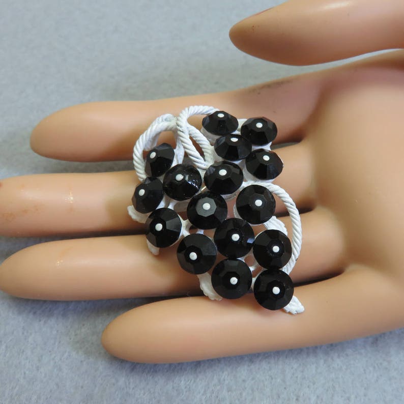 May include: A black and white brooch with a cluster of black round rhinestones set in a white metal frame.