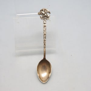 May include: A silver spoon with an eagle emblem at the top. The word "AMERICA" is engraved on the handle. The spoon has a rounded bowl and is likely a souvenir or collectible item.