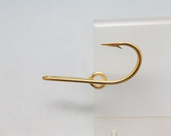 May include: A gold-colored fishing hook with a curved point and a straight shaft. The hook is designed with a circular loop where the line attaches. The hook is set against a white background.