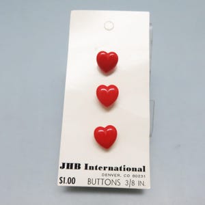 May include: Three bright red heart-shaped buttons, each measuring 3/8 inch, are displayed on a white card. The card includes the text "JHB International DENVER, CO 80231 BUTTONS 3/8 IN."